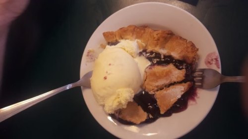 A slice of pie with berry filling topped with a scoop of vanilla ice cream on a white plate.