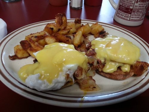 A plate of eggs Benedict with poached eggs and hollandaise sauce, served with crispy hash browns.