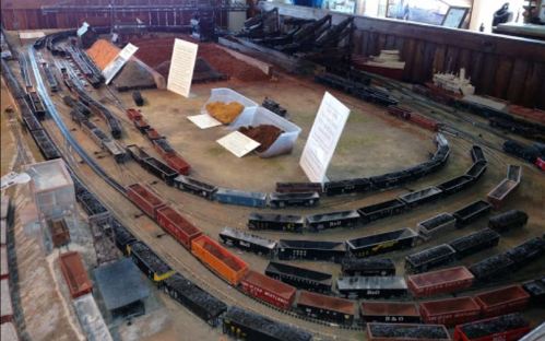 A model train layout featuring multiple tracks, freight cars, and informational signs in a display setting.