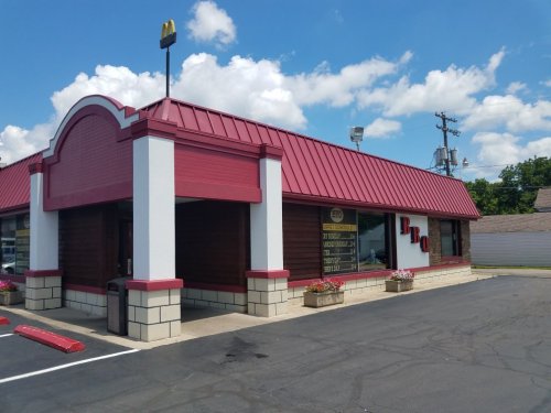 A fast-food restaurant with a red roof and white walls, featuring large windows and a BBQ sign. Clear blue sky above.