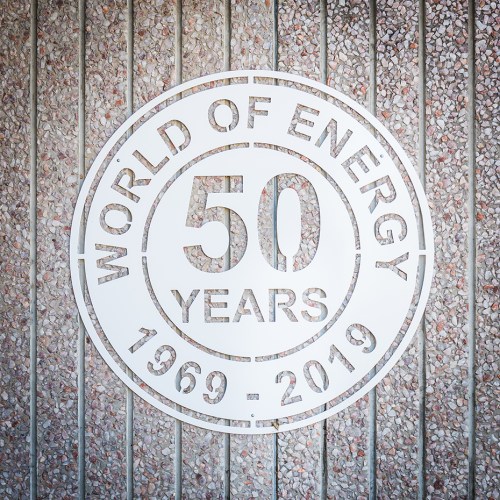 A circular metal sign reads "World of Energy 50 Years 1969 - 2019" against a textured wall.