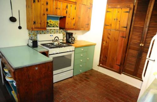 Cozy kitchen with wooden cabinets, a gas stove, and a green accent cabinet, featuring brick flooring and colorful tiles.
