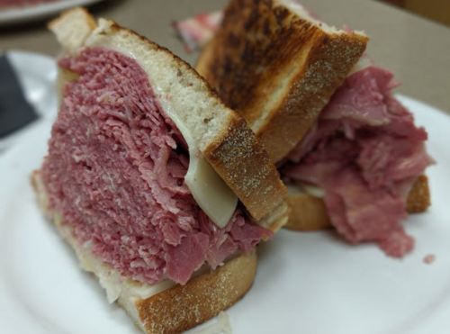 A close-up of a stacked sandwich with layers of pink corned beef and melted cheese between toasted bread slices.