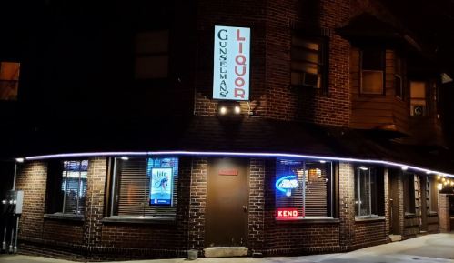 A brick building at night with a sign reading "Gunselman's Liquor" and illuminated windows showcasing various beer brands.