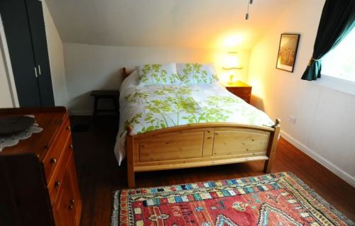 Cozy bedroom with a wooden bed, floral bedding, a nightstand, and a colorful rug under soft lighting.