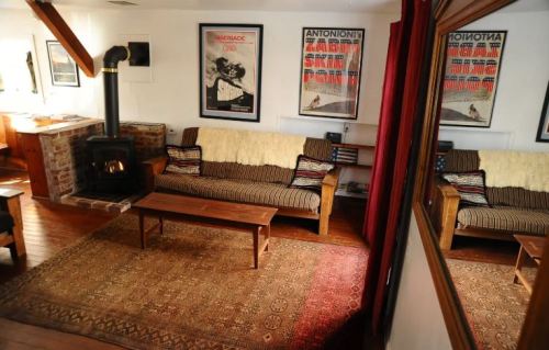 Cozy living room with a wooden stove, striped sofa, coffee table, and vintage posters on the walls. Warm, inviting atmosphere.