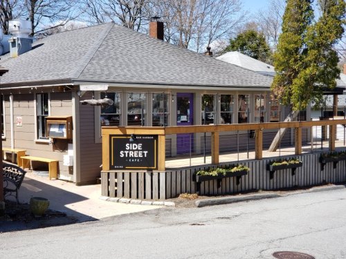 A cozy café with a wooden deck and sign reading "Side Street Café," surrounded by trees and a clear blue sky.