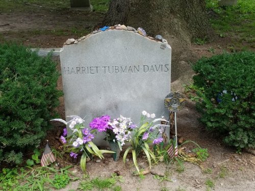 Grave marker for Harriet Tubman-Davis, surrounded by flowers and small flags, set in a grassy area.