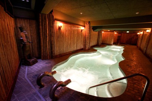 A serene indoor spa with a winding pool, bamboo walls, soft lighting, and a decorative statue.