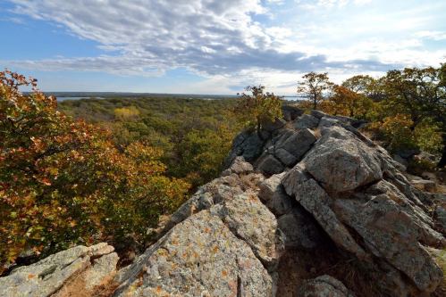 A rocky outcrop overlooks a lush landscape of trees and a distant body of water under a cloudy sky.