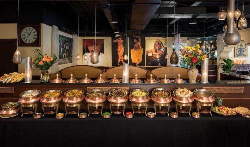 A buffet display with copper serving dishes filled with various dishes, set in a warmly lit restaurant with artwork and flowers.