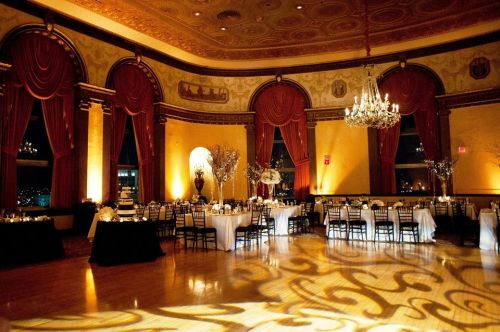 Elegant banquet hall with chandeliers, draped curtains, and tables set for an event, featuring warm lighting and decorative accents.