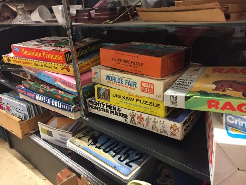 A shelf filled with vintage board games and puzzles, including "Hawaiian Princess" and "World's Fair Jigsaw Puzzle."