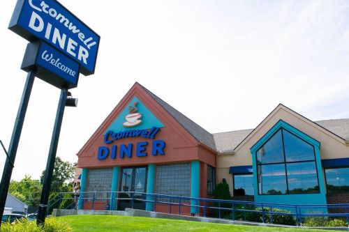 Exterior of Cromwell Diner with a blue sign, welcoming guests, and a modern building design under a clear sky.