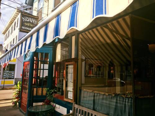 Exterior of Noah's Restaurant featuring blue and white striped awning, colorful doors, and a welcoming atmosphere.