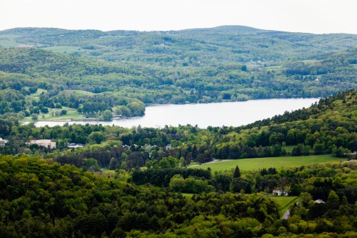 A scenic view of lush green hills surrounding a tranquil lake, with a small town visible in the foreground.