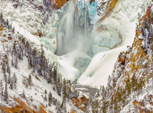 A stunning winter scene of a frozen waterfall surrounded by snow-covered cliffs and evergreen trees.