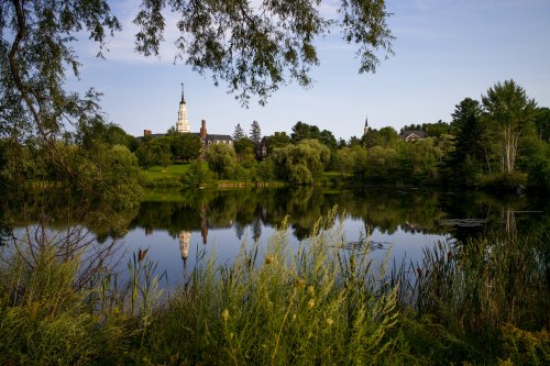 A serene landscape featuring a calm lake reflecting lush greenery and a historic building in the background.