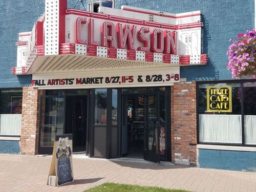 Exterior of Clawson with a marquee, featuring a market announcement and a café sign. Bright flowers adorn the entrance.
