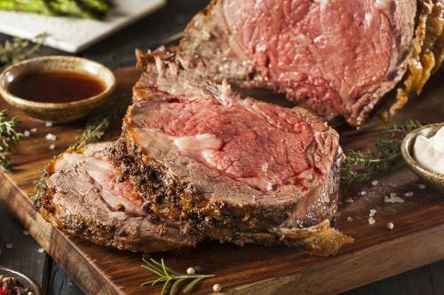 A close-up of a perfectly cooked prime rib roast, sliced to reveal juicy, pink meat, garnished with herbs.