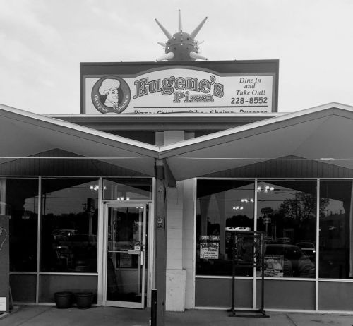 A black and white photo of Eugene's Pizza restaurant exterior with a sign and large windows.