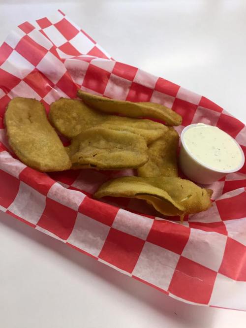 A basket of golden fried snacks on red and white checkered paper, accompanied by a small cup of dipping sauce.