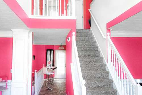 Brightly colored interior with pink walls, a staircase, and a small bar area. Natural light from a nearby door.