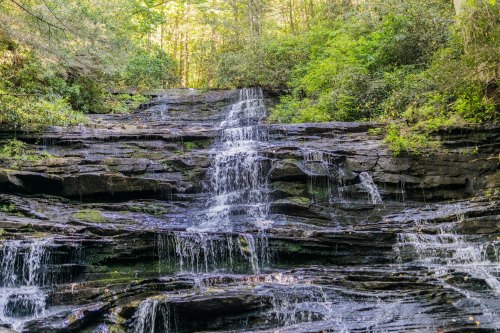 A serene waterfall cascading over rocky layers, surrounded by lush green foliage and trees.
