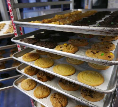 Trays of freshly baked cookies, including chocolate chip, oatmeal, and peanut butter, cooling on racks.