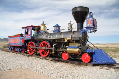 A vintage steam locomotive named "Jupiter" with red and blue accents, parked on a gravel track under a blue sky.