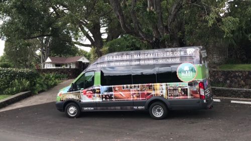 A colorful tour van parked in a lush, green area, promoting Maui Craft Tours with various images on its side.