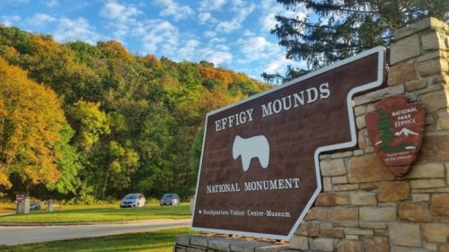 Sign for Effigy Mounds National Monument, surrounded by colorful trees and a clear blue sky.