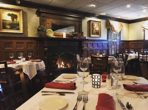 Elegant restaurant interior with wooden walls, a fireplace, and tables set with white linens and red napkins.