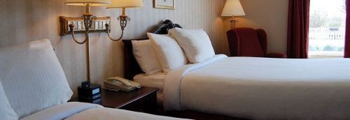 A cozy hotel room featuring two beds, a red armchair, bedside lamps, and a phone on a wooden nightstand.