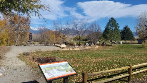 A scenic park with autumn foliage, a statue, and mountains in the background under a blue sky with clouds.