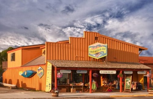 A colorful outdoor shop with a wooden facade, displaying gear and clothing, set against a cloudy sky.