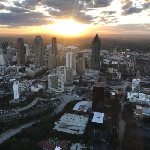 Aerial view of a city skyline at sunset, with buildings and roads illuminated by warm golden light.
