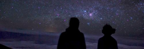Silhouettes of two people gazing at a starry night sky filled with vibrant stars and galaxies.