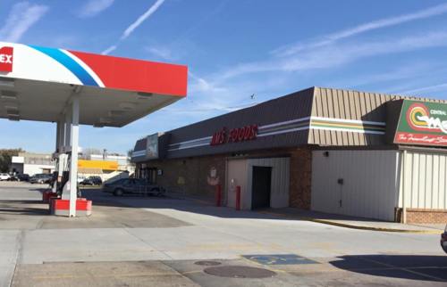 A gas station and a grocery store with a sign reading "M's Foods" in a suburban area on a clear day.
