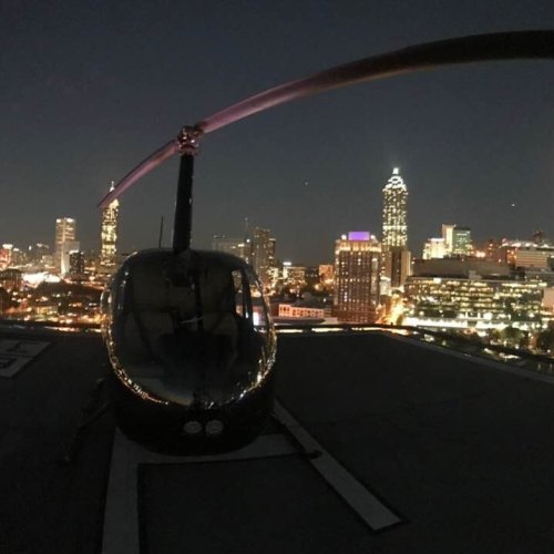 A helicopter on a rooftop at night, with a city skyline illuminated in the background.