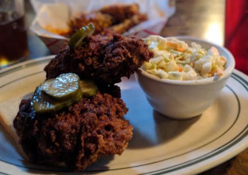 Two pieces of fried chicken topped with pickles, served with a side of coleslaw on a plate.