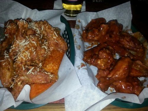Two baskets of chicken wings: one with a spicy sauce and grated cheese, the other coated in a rich, red sauce.