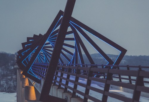 A modern bridge with striking blue lights, set against a winter landscape and a gray sky.