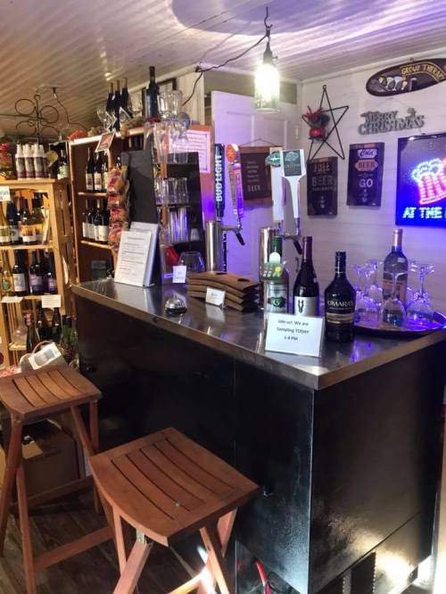 A cozy bar setup with wooden stools, bottles on shelves, and a glowing sign, creating a welcoming atmosphere.