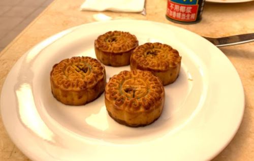 Four round, golden-brown mooncakes with intricate designs on a white plate.