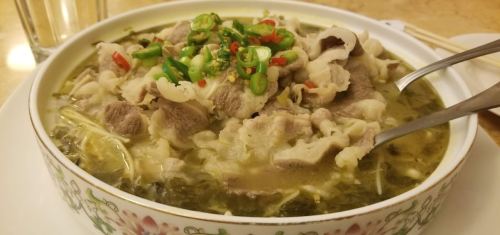 A bowl of soup with thinly sliced meat, green onions, and red chili peppers, garnished with herbs.