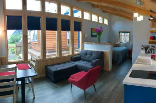 Cozy interior of a modern cabin featuring a living area, dining table, and a bedroom with large windows and natural light.