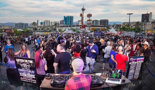 A lively outdoor event in Las Vegas with a DJ, large crowd dancing, and city skyline in the background.