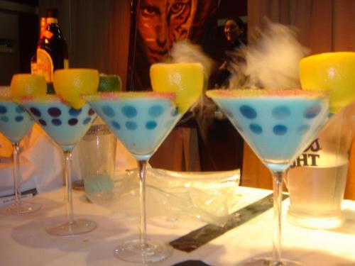 Colorful cocktails in tall glasses, featuring blue liquid, fruit garnishes, and a smoky effect.