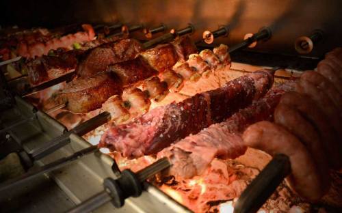 Grilled meats on skewers cooking over an open flame, showcasing a variety of cuts and textures.